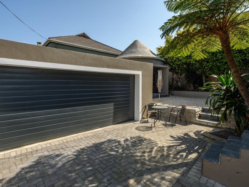 Front exterior view featuring a modern automated garage door, paved driveway, and landscaped stone retaining walls with steps leading to the entrance.