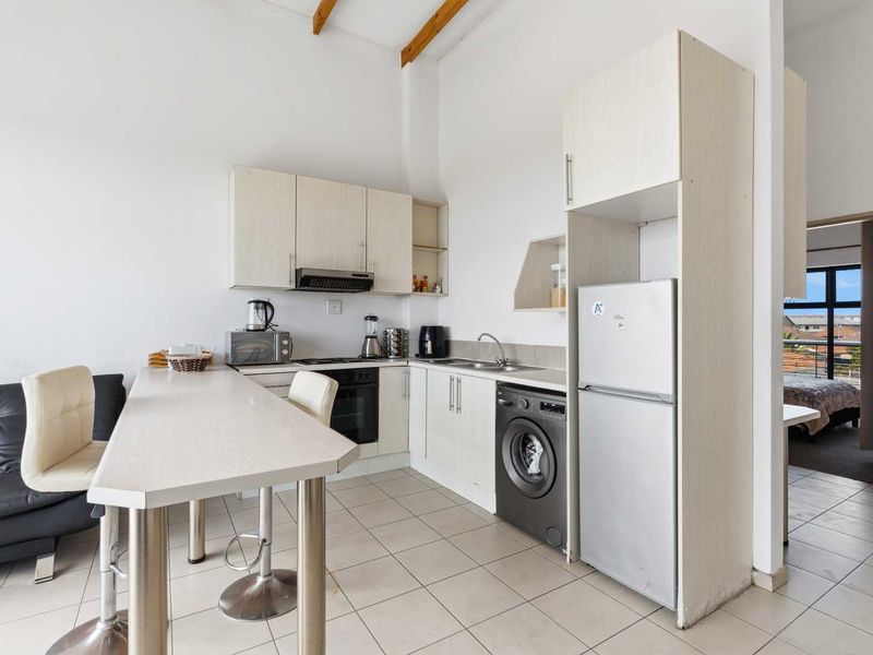 Compact kitchen featuring light-toned cabinetry, laminate countertops, integrated appliances, tiled flooring, and exposed timber ceiling beams, offering a functional and bright workspace.