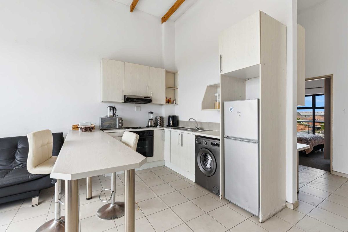 Compact kitchen featuring light-toned cabinetry, laminate countertops, integrated appliances, tiled flooring, and exposed timber ceiling beams, offering a functional and bright workspace.