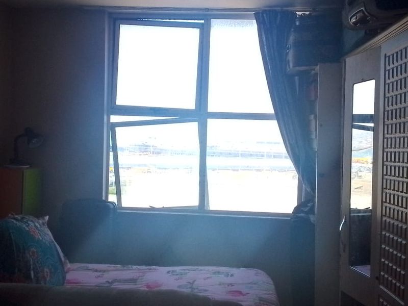 A bedroom featuring a large window with a view and a built-in wardrobe. The room requires maintenance due to a damaged window pane.