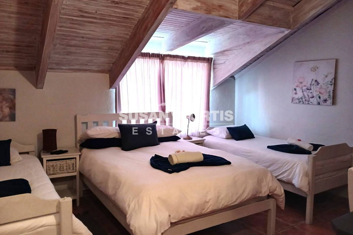 A bedroom featuring a vaulted timber-beamed ceiling, tiled flooring, and a window with curtains, providing a rustic and cozy atmosphere.