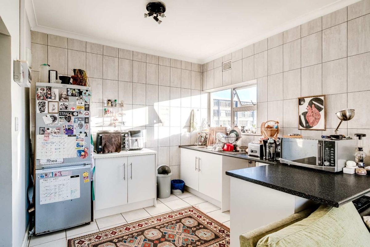 A functional kitchen featuring white cabinetry, dark countertops, and full-height wall tiling, offering a practical layout with natural light from the window.