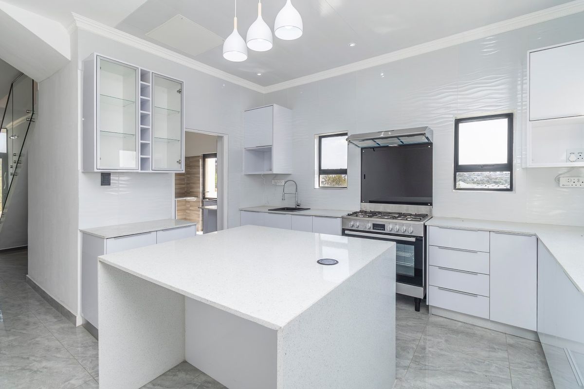 Modern, bright kitchen featuring a central island, quartz countertops, gas stove with extractor, and sleek white cabinetry with glass-fronted display units.