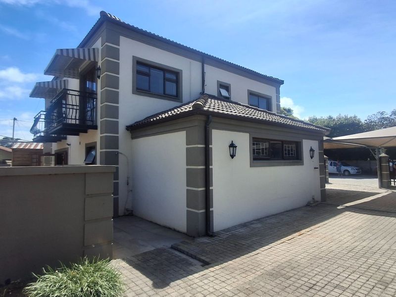 A well-maintained double-story residential property featuring a paved driveway, carport, and a balcony with wrought iron railings.