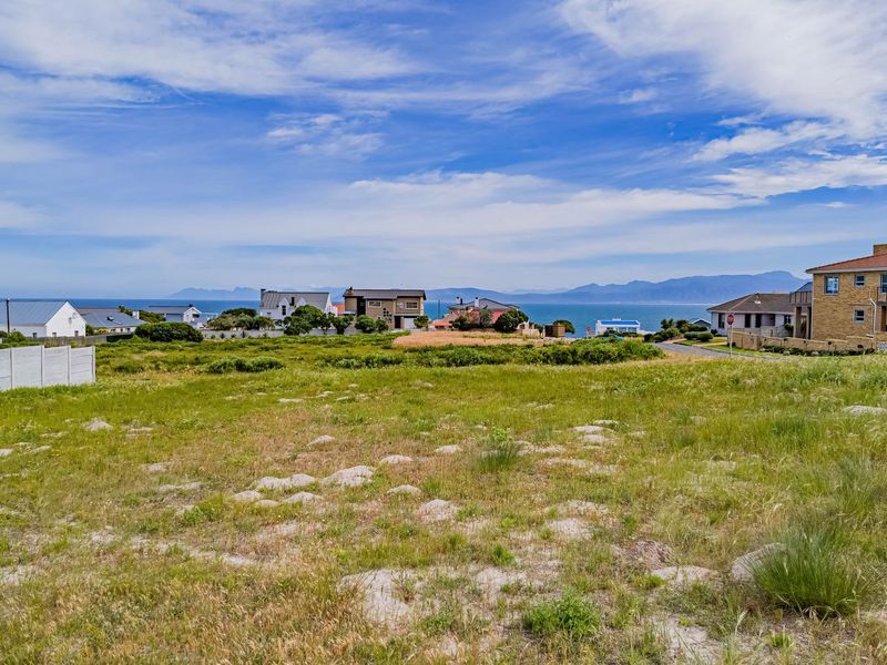 A wide-angle view of a vacant residential plot overlooking a coastal neighborhood with distant mountain and ocean vistas.