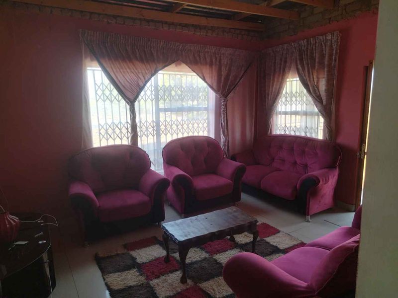 Living room featuring tiled flooring, security gates on windows, and exposed timber ceiling beams with unfinished brickwork.