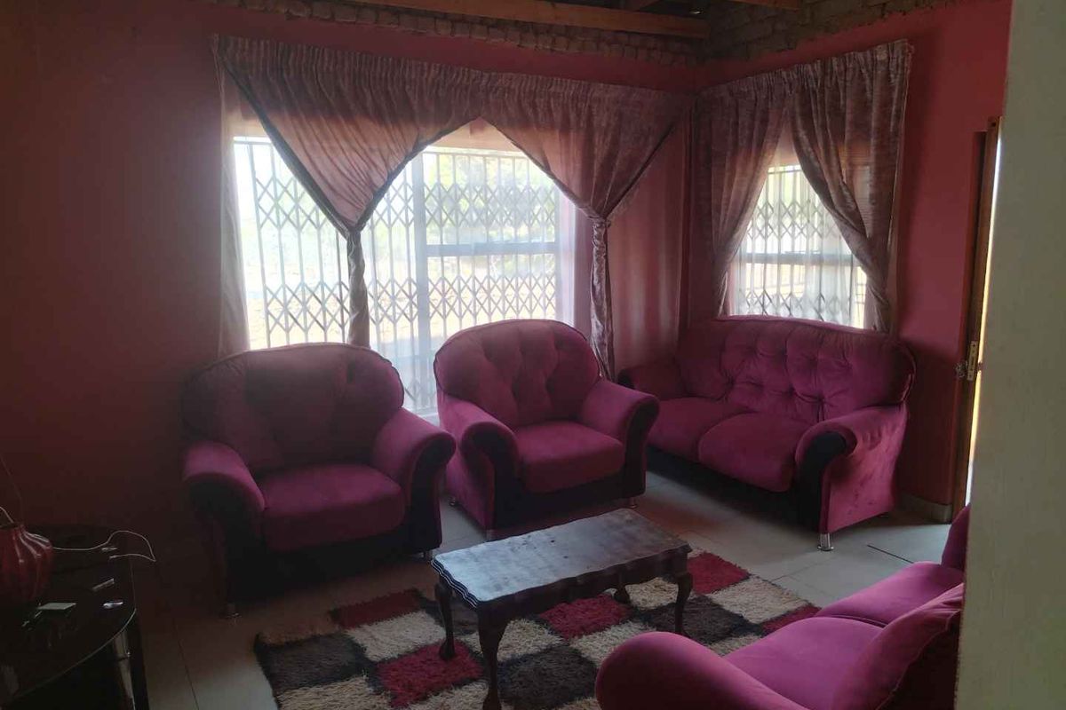 Living room featuring tiled flooring, security gates on windows, and exposed timber ceiling beams with unfinished brickwork.