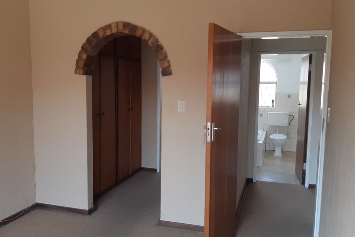 A bedroom featuring built-in cupboards, a decorative brick archway, and direct access to an en-suite bathroom.