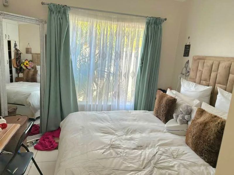 A bedroom featuring tiled flooring and built-in cupboards, with natural light entering through a window dressed with curtains.