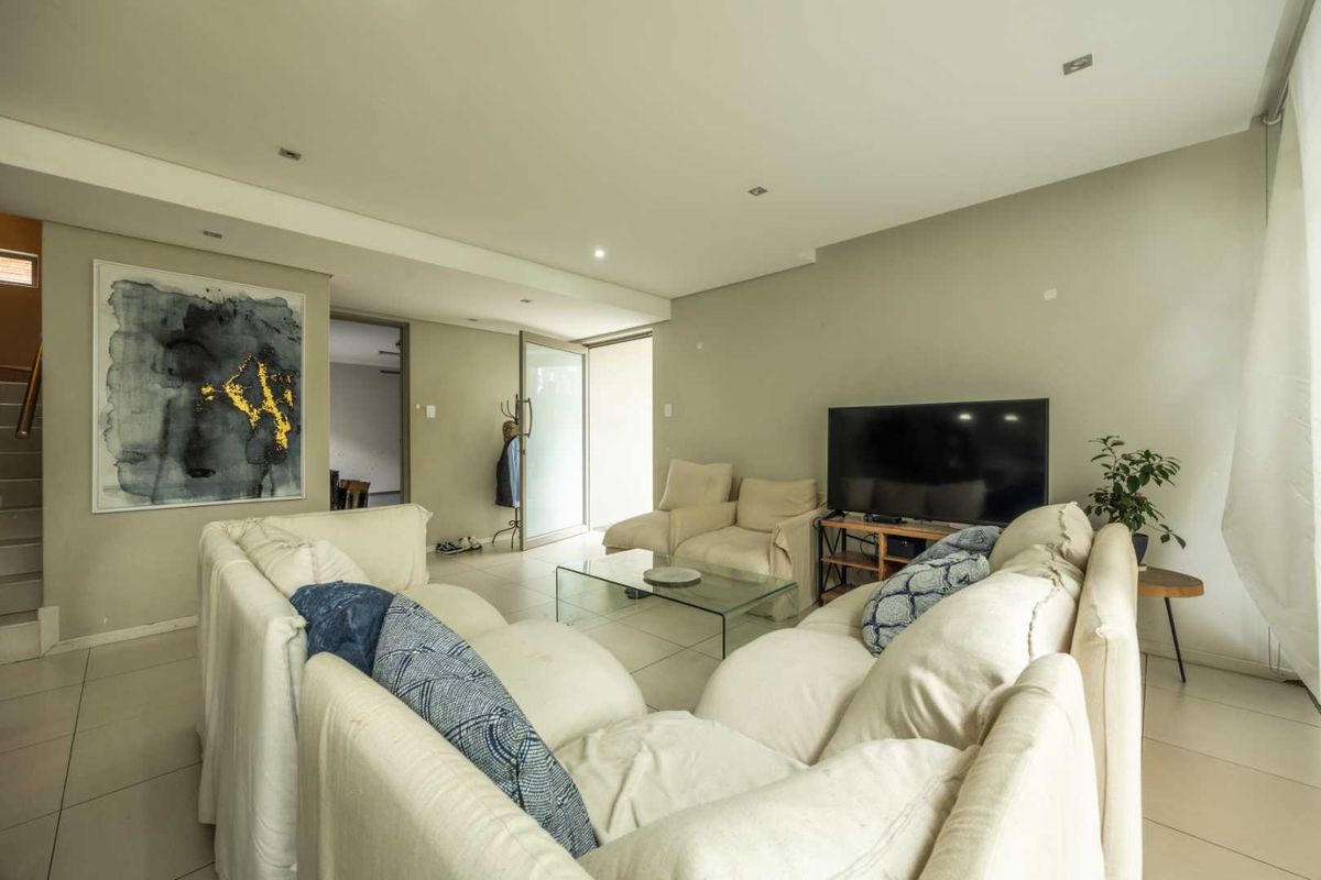 A spacious living room featuring neutral tiled flooring, recessed downlighting, and a glass door leading to an adjacent area.