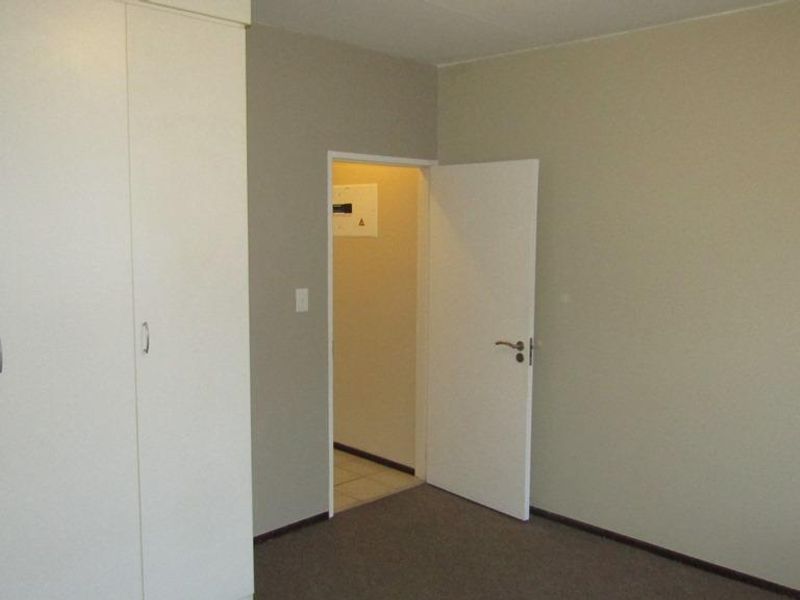 A vacant bedroom featuring built-in cupboards, neutral wall finishes, and carpeted flooring, with an adjacent hallway visible through the doorway.