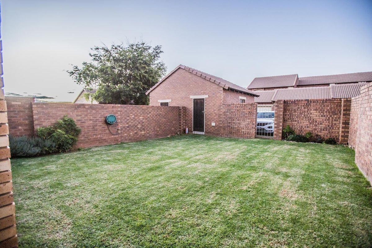 A private rear garden featuring a well-maintained lawn, enclosed by brick boundary walls and including a detached brick outbuilding.