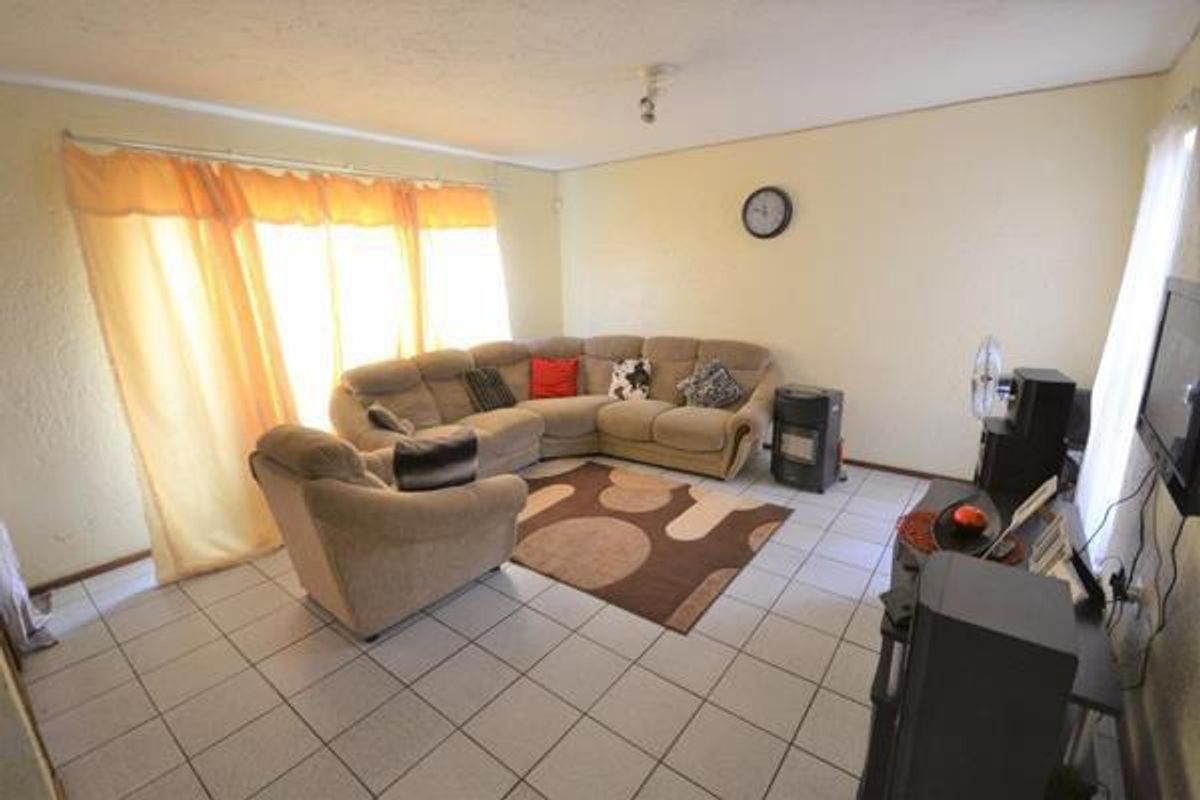 A spacious living room featuring tiled flooring, large windows with natural light, and a neutral wall finish, providing a comfortable and functional living space.