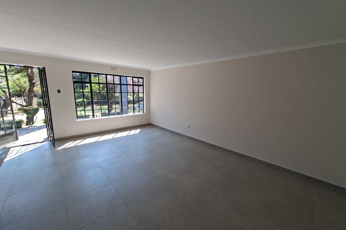 A bright, empty living room featuring neutral tiled flooring, coved ceilings, and large steel-framed windows with access to the exterior.