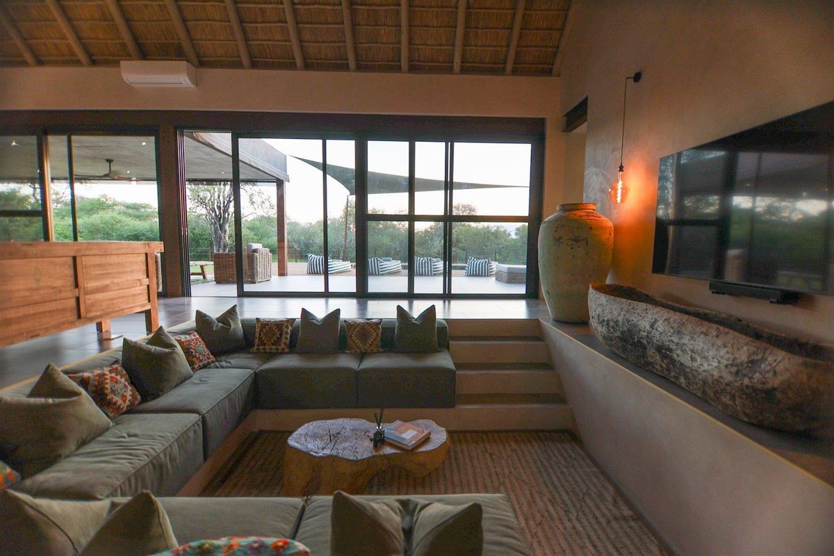 Spacious sunken living area featuring a high thatched ceiling, large sliding glass doors opening to a patio, and integrated wall-mounted television.