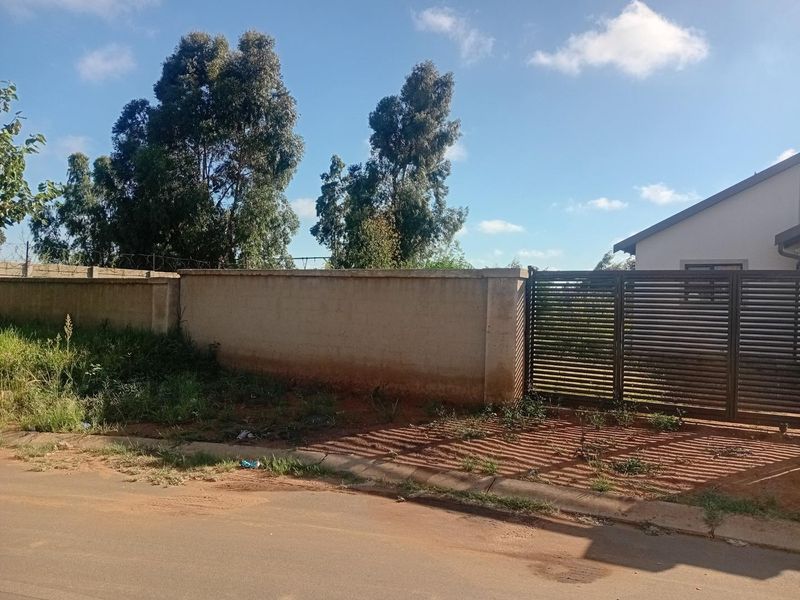 Front view of the property featuring a perimeter wall, metal sliding gate, and barbed wire security fencing along the street boundary.