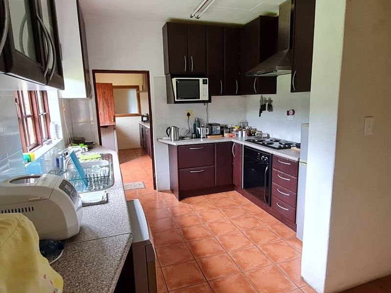 A functional kitchen featuring dark wood cabinetry, laminate countertops, a built-in oven with gas hob, and tiled flooring, offering a practical workspace.