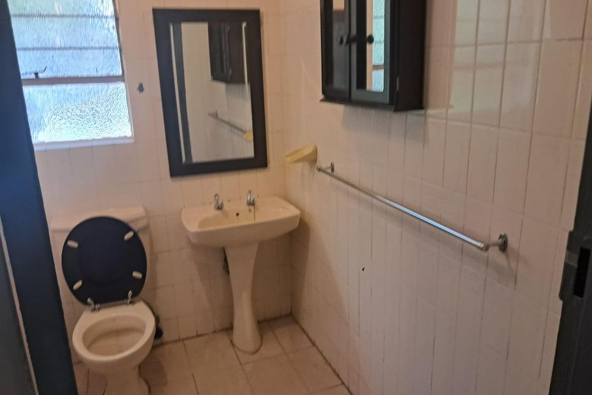 A dated bathroom featuring a pedestal sink, standard toilet, and wall-mounted cabinetry with tiled walls and flooring.