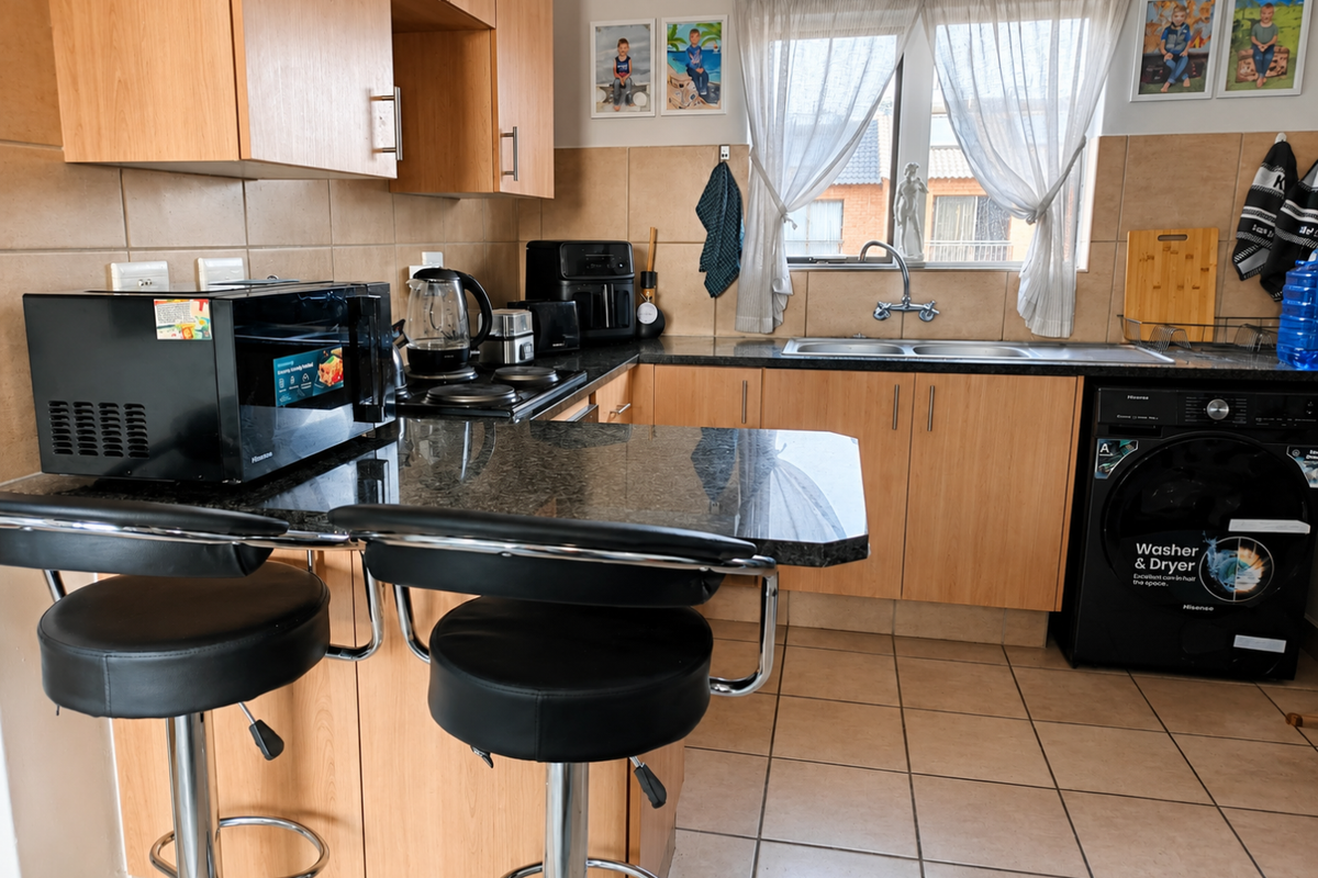 A functional kitchen featuring laminate cabinetry, granite countertops, a double basin sink, and integrated laundry appliances with ceramic tile finishes throughout.