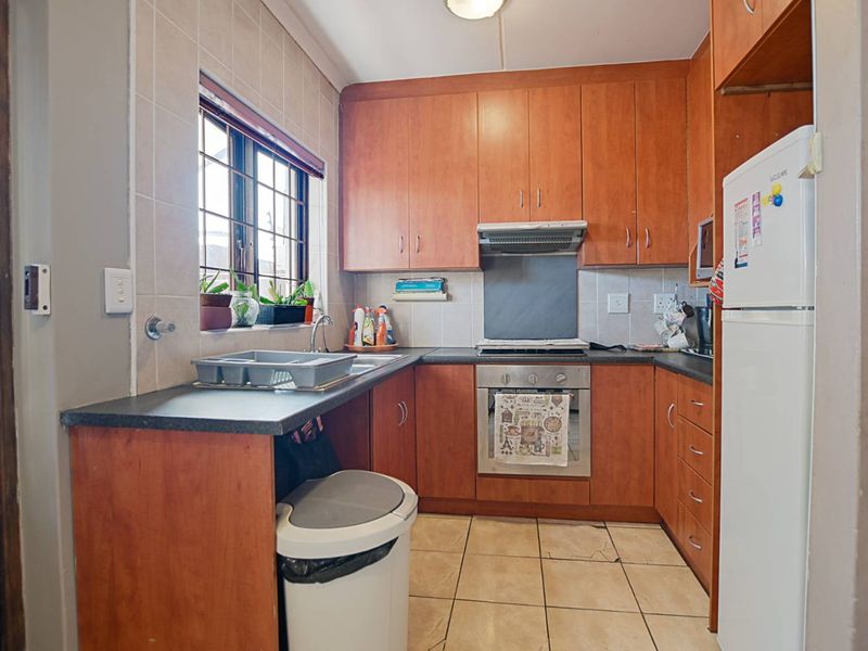A functional kitchen featuring wood-finish cabinetry, built-in oven with extractor fan, tiled backsplash, and durable ceramic flooring.