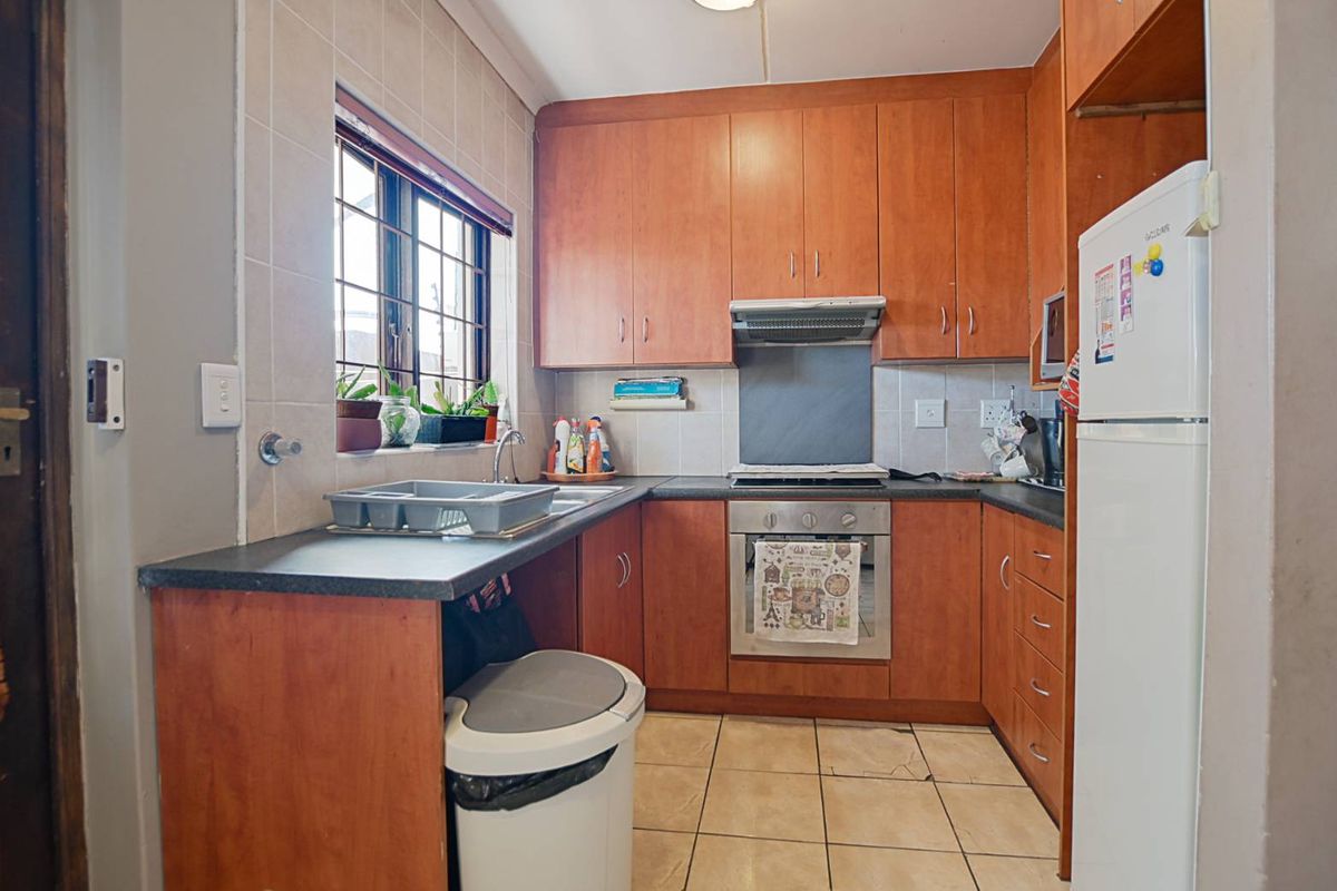 A functional kitchen featuring wood-finish cabinetry, built-in oven with extractor fan, tiled backsplash, and durable ceramic flooring.