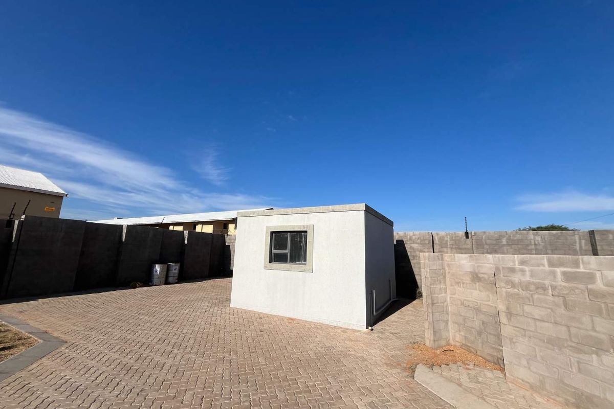 A view of a paved backyard area featuring a small, modern outbuilding enclosed by high perimeter walls.