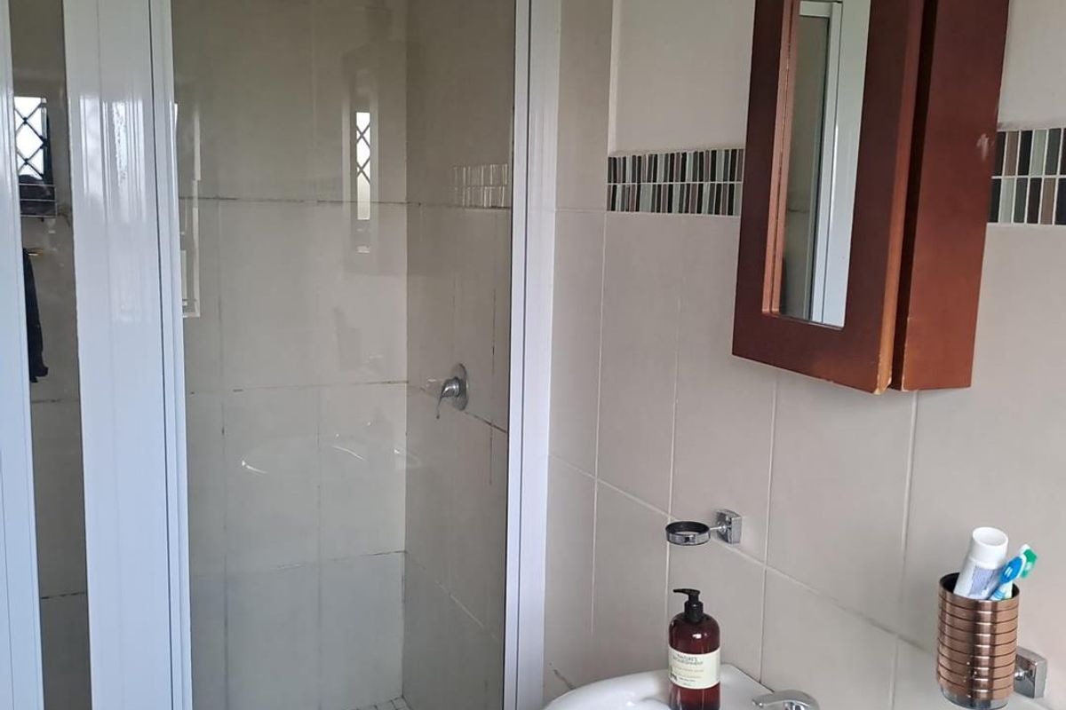 A functional bathroom featuring a shower enclosure with a white frame, a pedestal basin with a mixer tap, and a wall-mounted medicine cabinet.