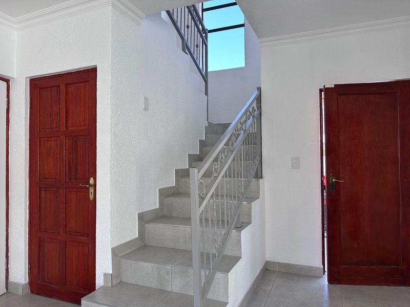 A bright, clean hallway featuring a tiled staircase with a decorative wrought iron balustrade and classic solid wood doors.