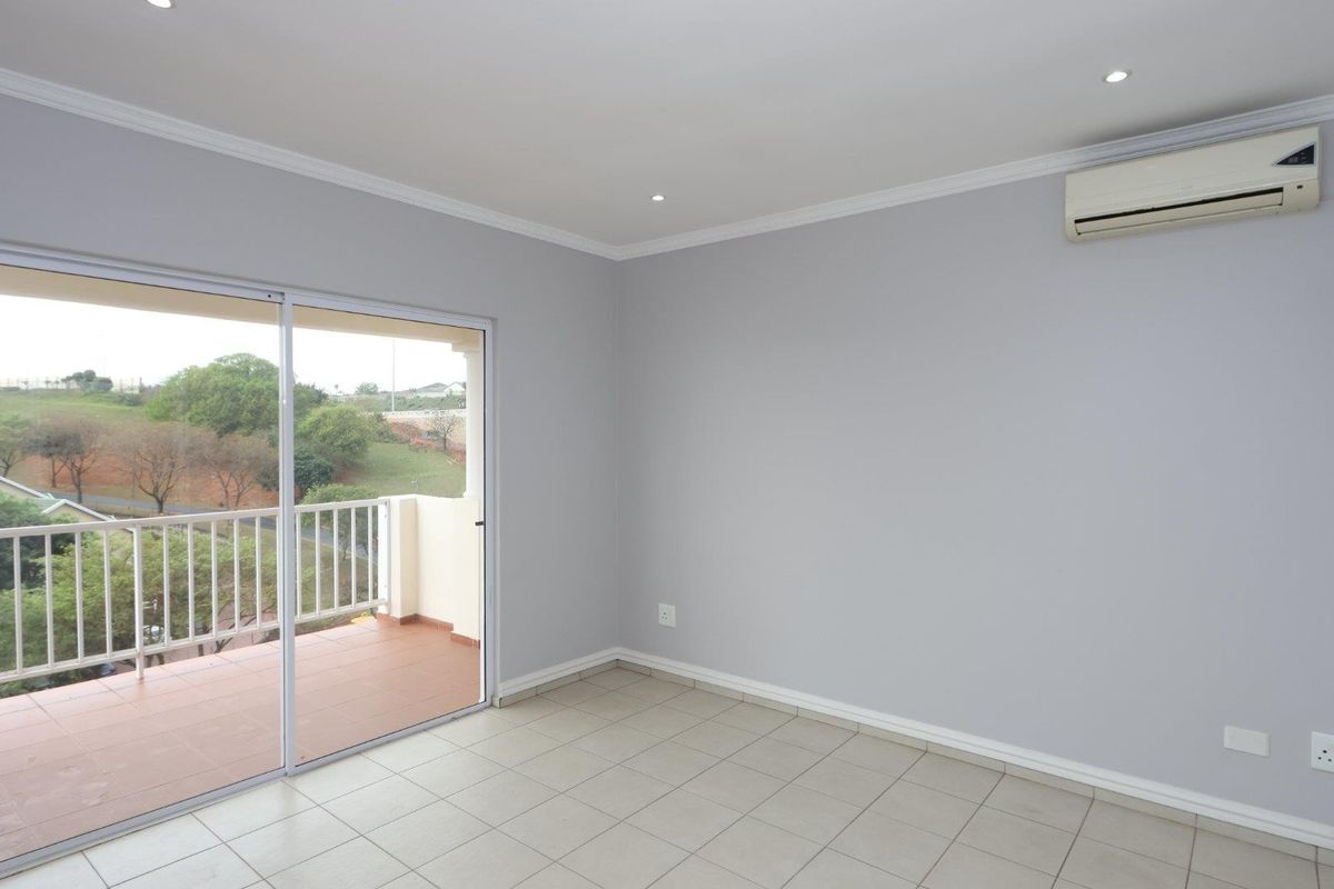 A bright, empty living room featuring neutral tiled floors, recessed lighting, an air conditioning unit, and a sliding door leading to a private balcony.