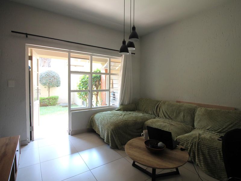 A bright living room featuring tiled floors, textured walls, and a large glass sliding door providing direct access to a private garden area.