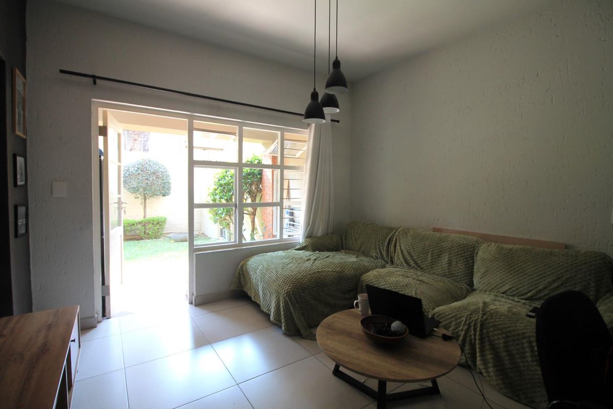 A bright living room featuring tiled floors, textured walls, and a large glass sliding door providing direct access to a private garden area.