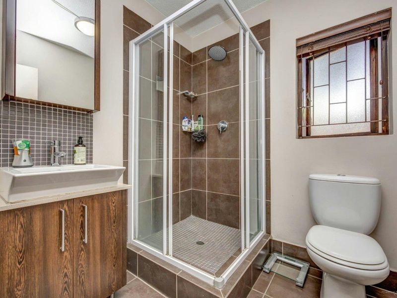 A functional bathroom featuring a shower enclosure, vanity cabinet with basin, and toilet, finished with tiled accents and a window with security bars.