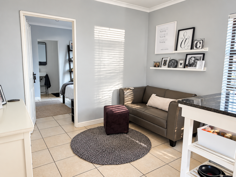 A well-maintained living area featuring neutral wall tones, tiled flooring, and natural light filtering through venetian blinds, with an open doorway leading to an adjacent room.