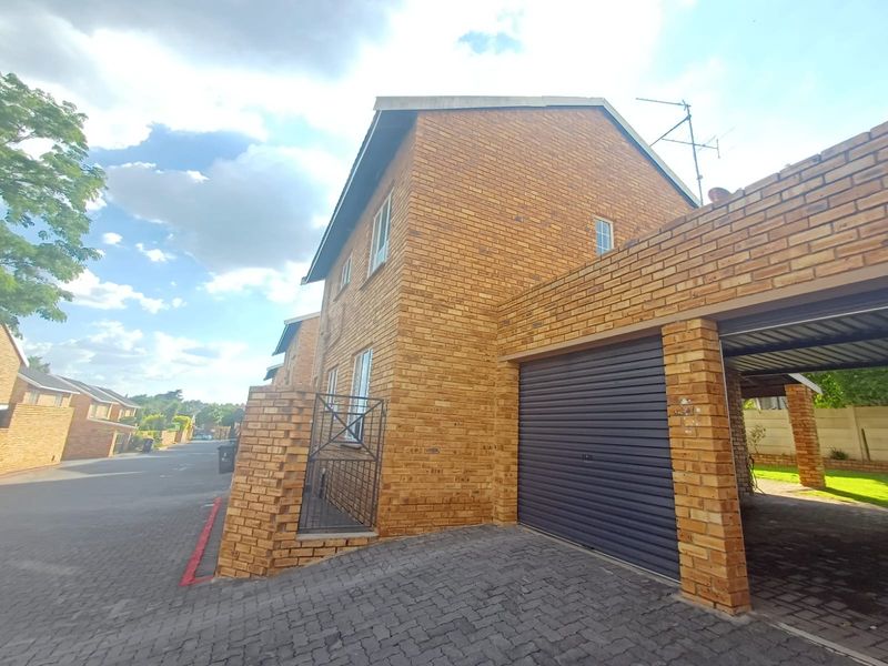Exterior view of a face brick townhouse featuring a paved driveway, roller garage door, and integrated carport.