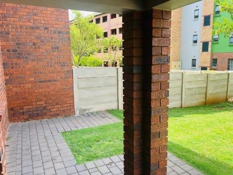 A covered patio area featuring brick pillars and paving, overlooking a small private garden space with a precast concrete boundary wall.