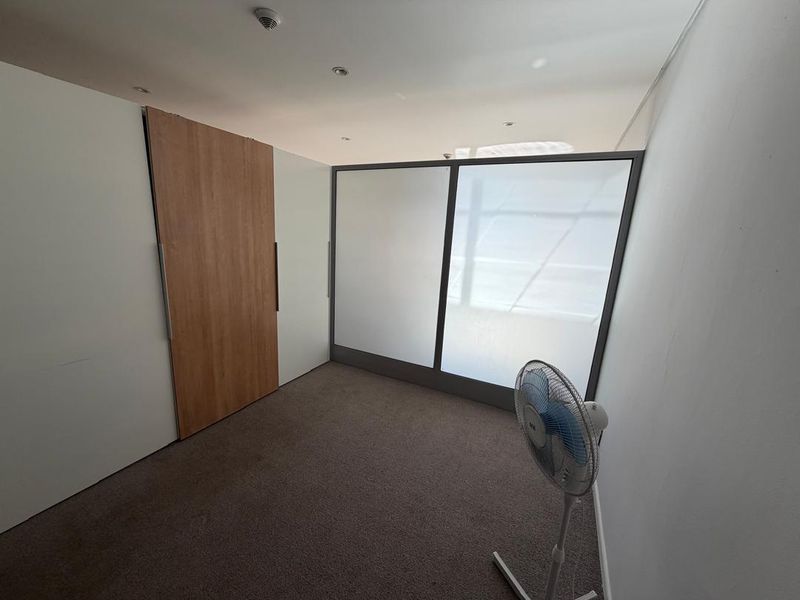 A bright, empty bedroom featuring neutral carpet flooring, built-in cupboards with wood-finish detailing, and a modern frosted glass partition.