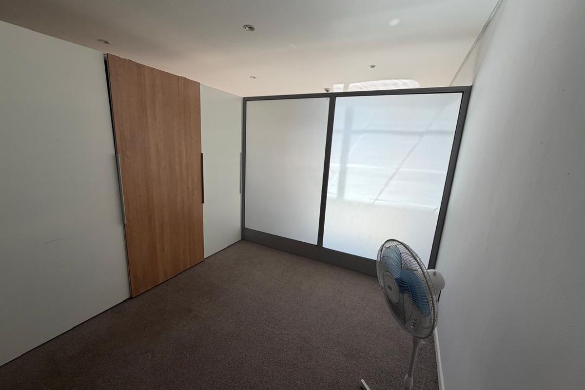 A bright, empty bedroom featuring neutral carpet flooring, built-in cupboards with wood-finish detailing, and a modern frosted glass partition.