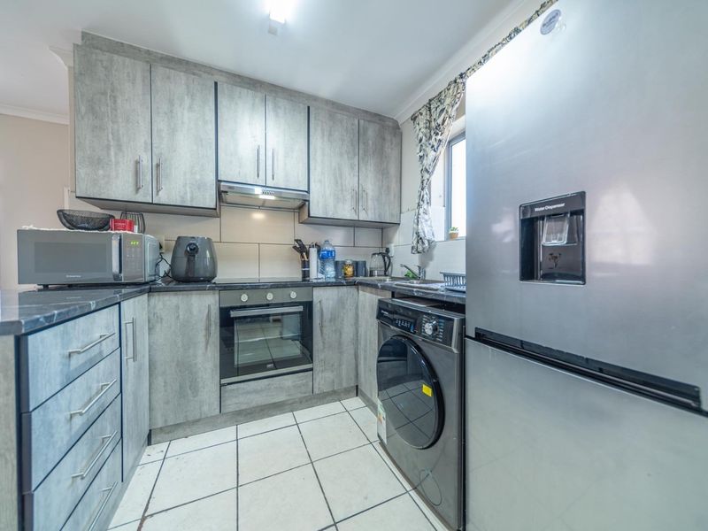 A functional kitchen featuring modern grey wood-look cabinetry, tiled flooring, a built-in oven, and a tiled backsplash.