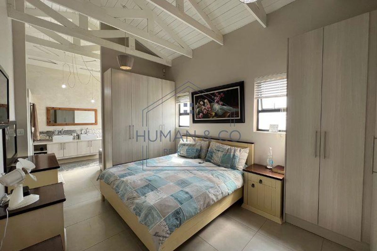 Spacious bedroom featuring high vaulted ceilings with exposed beams, built-in cabinetry, and an open-plan en-suite bathroom with dual vanity.