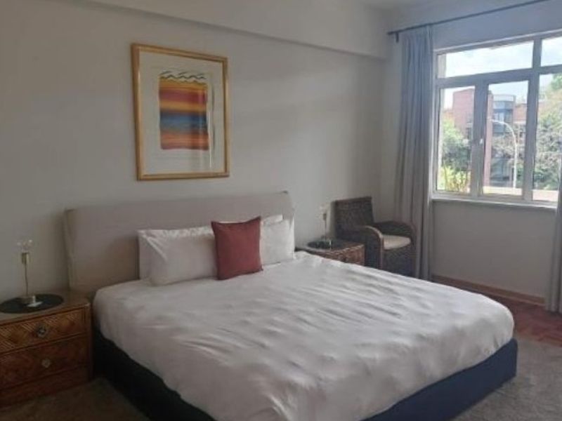 A well-lit bedroom featuring a large window with natural light, neutral wall finishes, and ample space for a double bed.