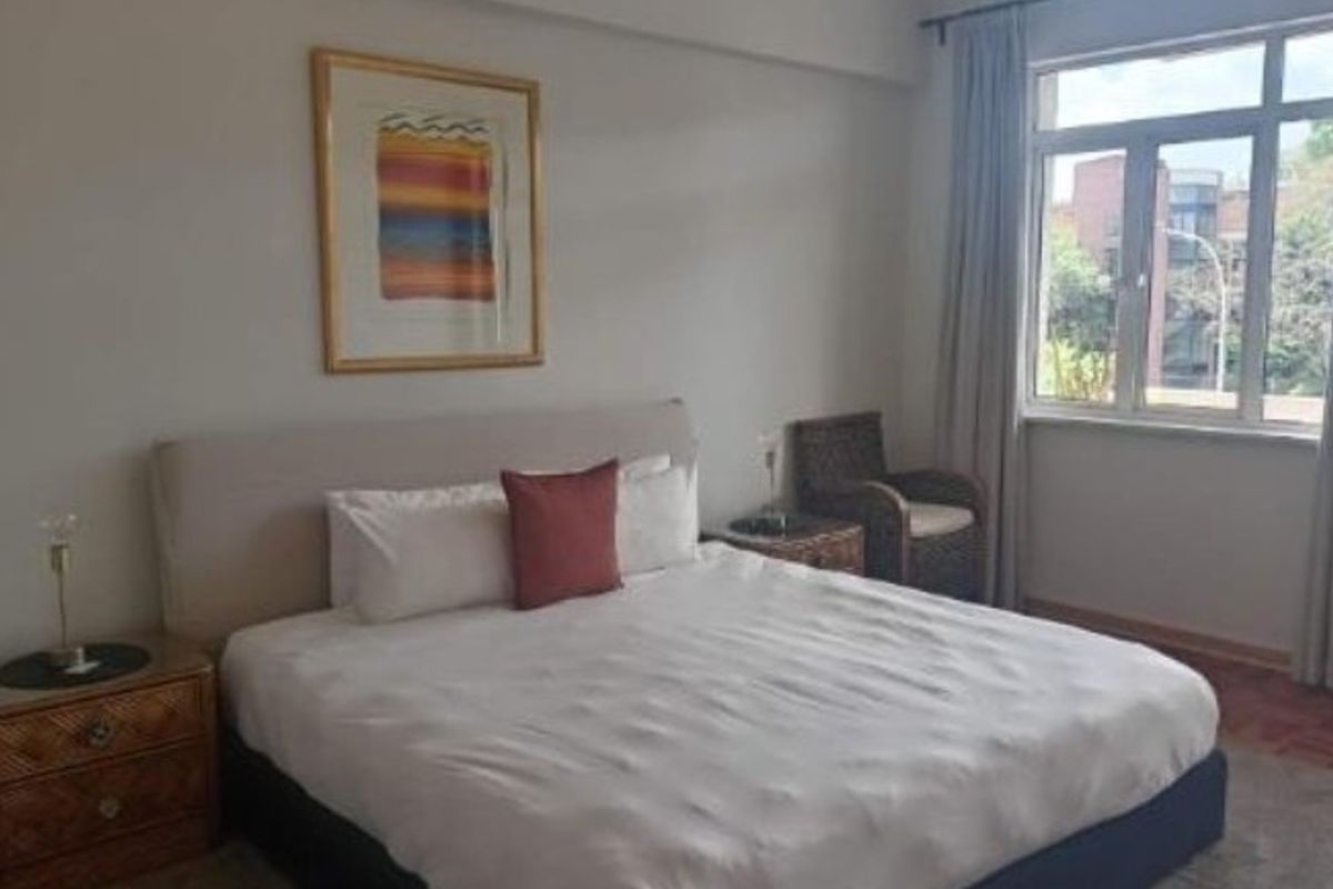 A well-lit bedroom featuring a large window with natural light, neutral wall finishes, and ample space for a double bed.