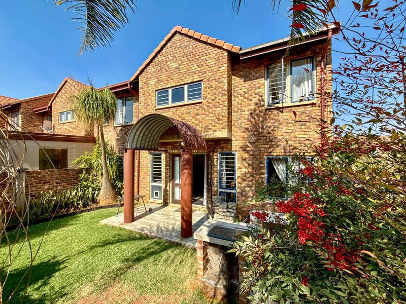 Rear view of a face brick townhouse featuring a paved patio, arched entrance canopy, and a built-in brick braai area set within a private garden.