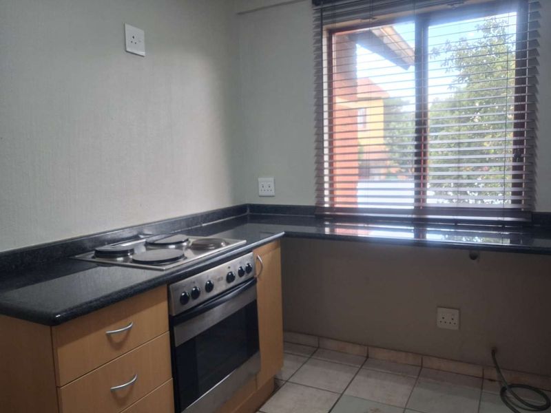 A functional kitchen featuring granite countertops, built-in oven, electric hob, and light wood cabinetry, complemented by tiled flooring and window blinds.