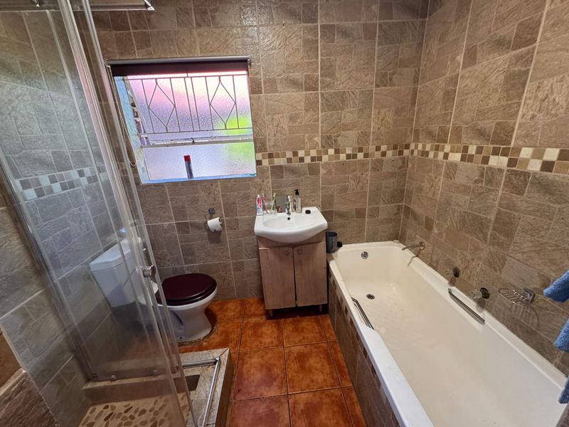 A functional bathroom featuring a shower enclosure, bathtub, vanity basin, and toilet, finished with full-height wall tiling and floor tiles.