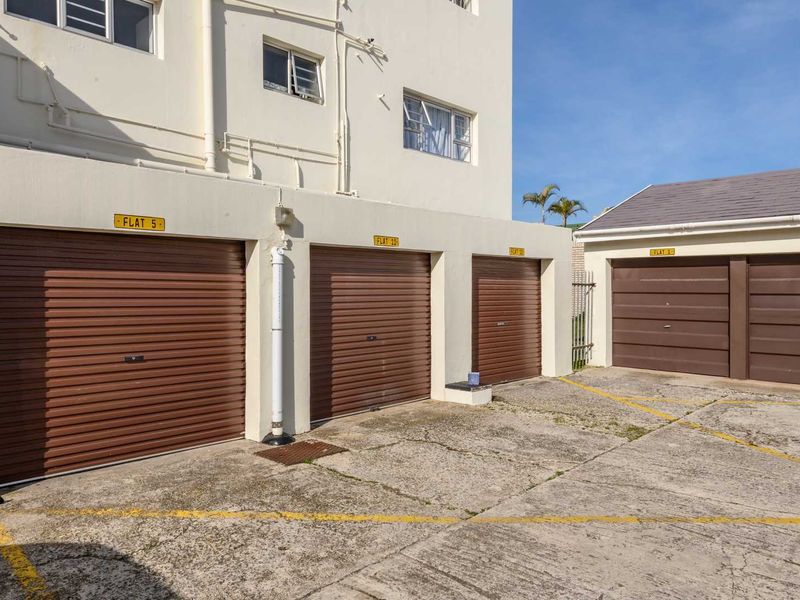 A row of secure roller shutter garages with a concrete driveway area, providing dedicated parking for the apartment complex.