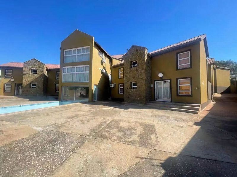 Rear exterior view of a multi-story residential building featuring a paved courtyard, swimming pool, stone facade accents, and multiple sliding glass door entrances.