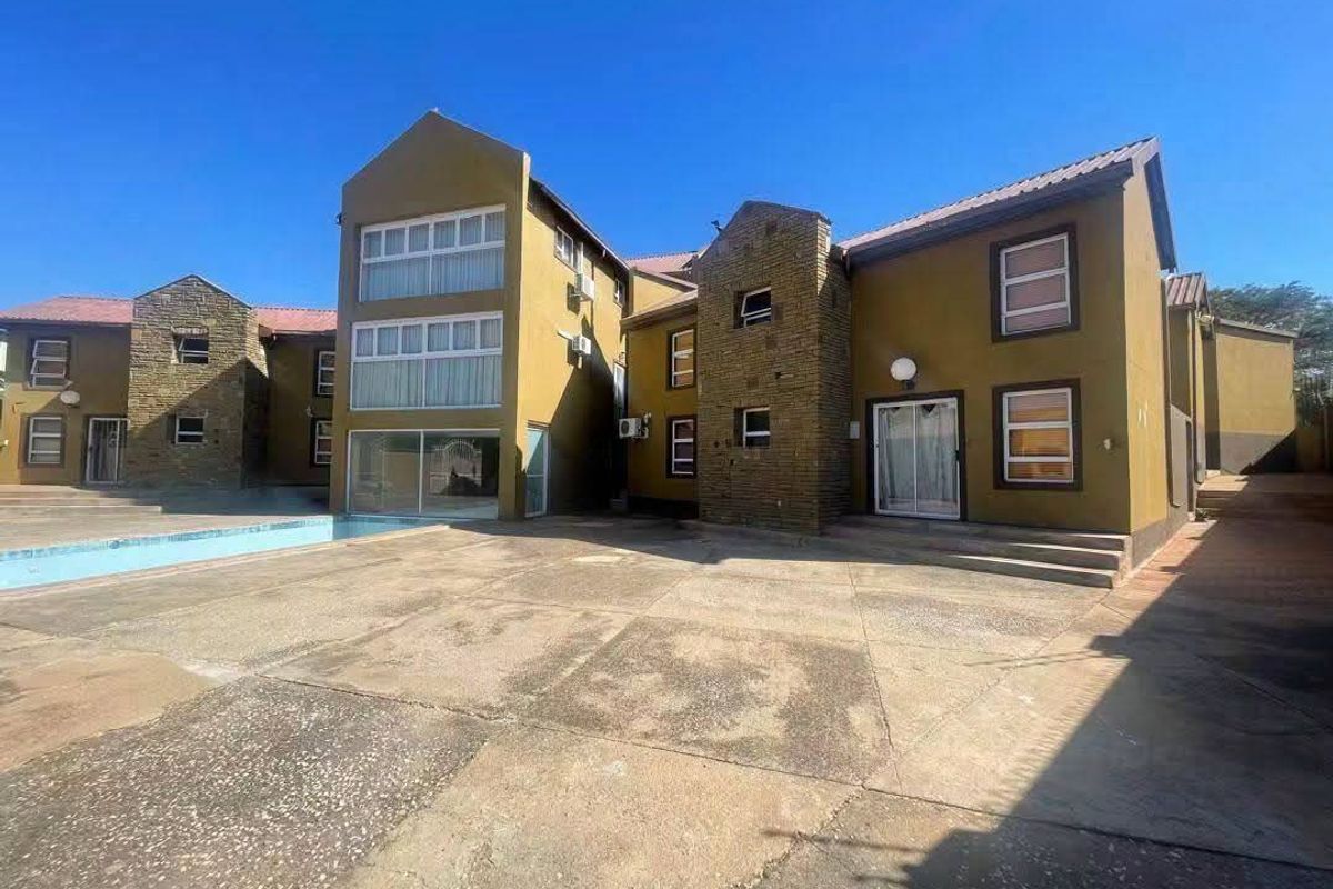 Rear exterior view of a multi-story residential building featuring a paved courtyard, swimming pool, stone facade accents, and multiple sliding glass door entrances.
