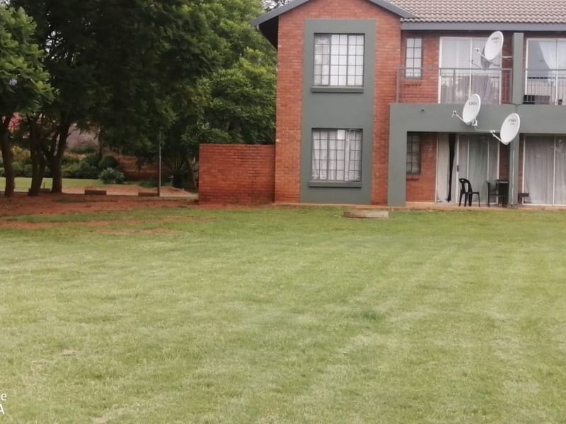 Rear view of a two-story brick apartment building featuring balconies, sliding glass doors, and a spacious communal lawn area.