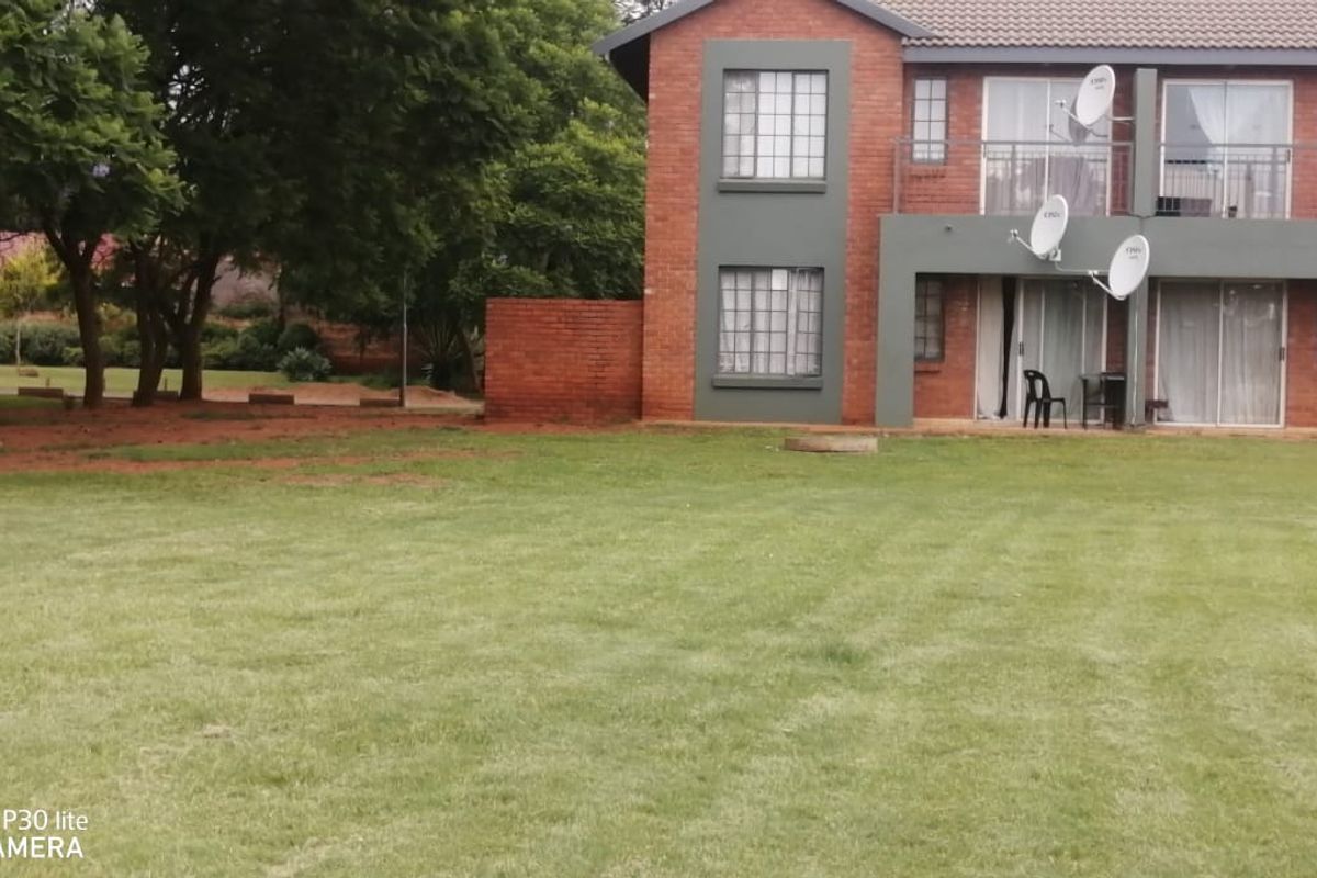Rear view of a two-story brick apartment building featuring balconies, sliding glass doors, and a spacious communal lawn area.