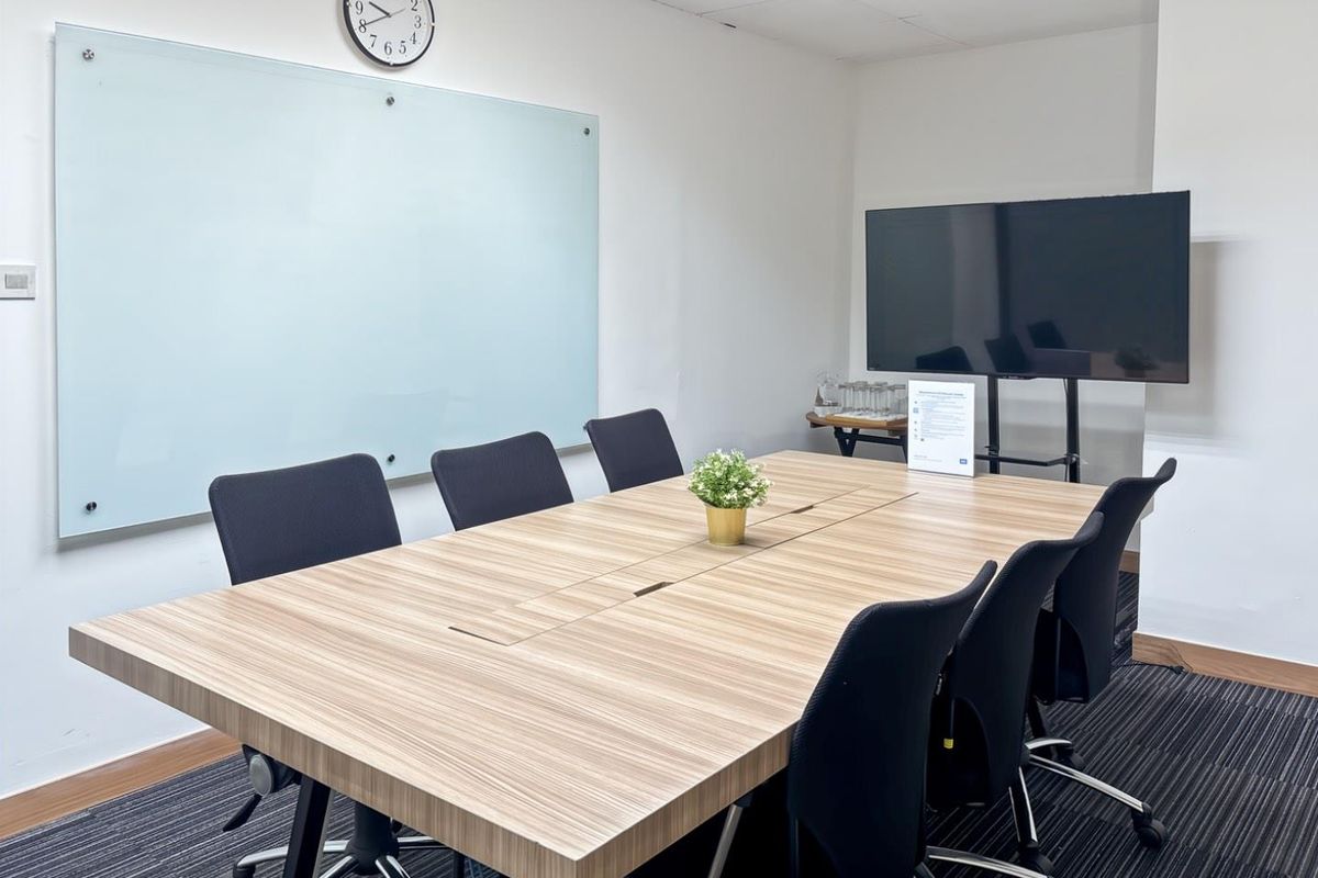 A professional office meeting room featuring a large glass whiteboard, carpeted flooring, and recessed ceiling ventilation.